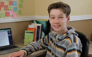 Student smiling at the camera while working with his laptop